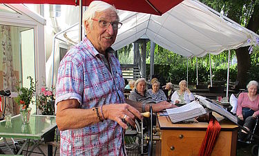 Leonhard Gutmair steht an seiner Drehorgel und unterhält die Bewohnerinnen. 